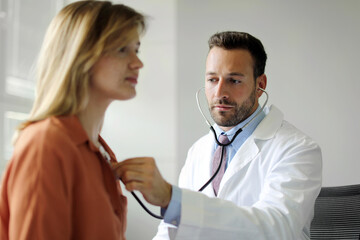 Male doctor using stethoscope, listening to female patient's breath or heartbeat, woman coming to...