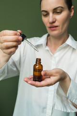 A smiling woman holds a brown bottle of essential oil in her hands and with a pipette.