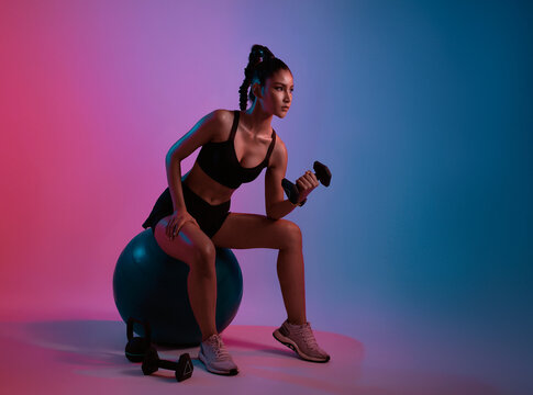 Workout. young asian woman doing weightlifting exercise with dumbbell in fitness studio neon background.