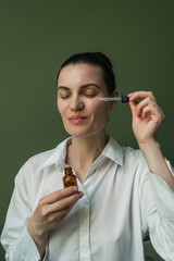 A nice woman with clean skin should apply oil, essence from a pipette to her face.