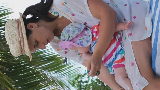 Vertical video. Mother applying sunscreen lotion on her baby on tropical beach
