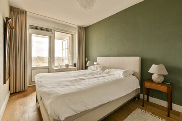 a bedroom with green walls and white bedding, wooden flooring and large windows overlooking the cityscapea