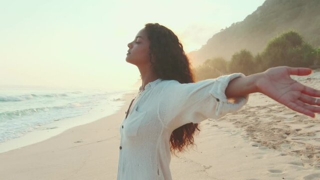 Young carefree attractive Indian woman is stands on beach and spreading arms to sides enjoys last rays of evening sun illuminating sea coast of tourist island. Vacation, holidays, weekend