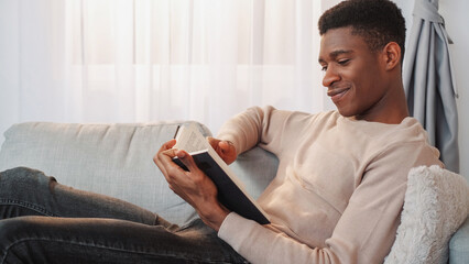 Book relaxing. Reading leisure. Domestic comfort. Peaceful cheerful man enjoying cozy weekend with literature novel bestseller story on sofa at home.