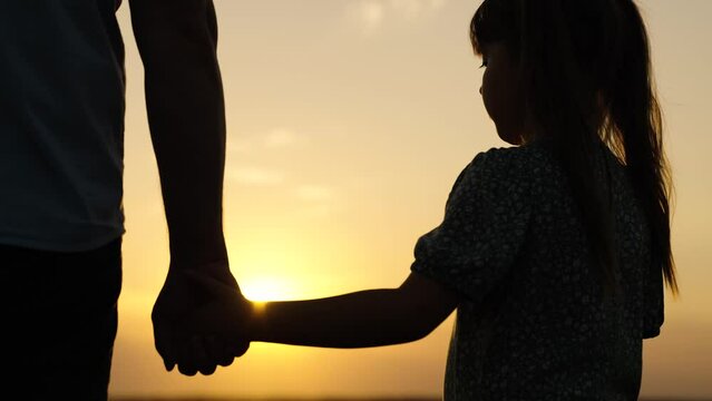 Concept of fathers care for child. Little daughter, dad hold hands closeup, nature, sun. Happy family, teamwork. Adoption of child. Parent, kid girl outing together. family trust concept. Silhouette