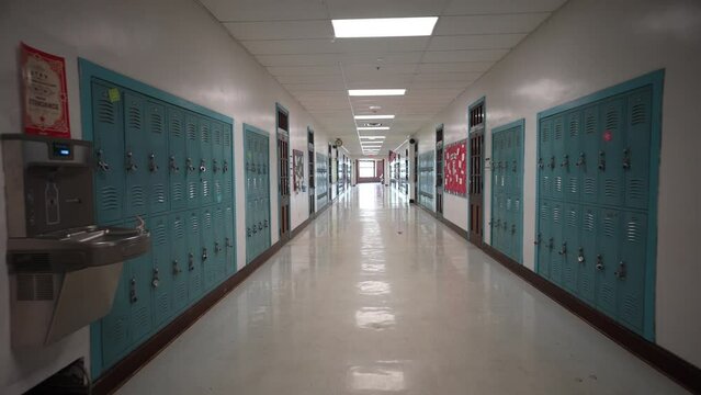 Wide angle push in down a long empty high school hallway with US American flag with corridor lined with student lockers.