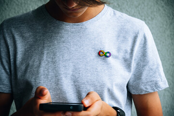 Teenage boy with autism infinity rainbow symbol sign metallic pin brooch on t-shirt using...