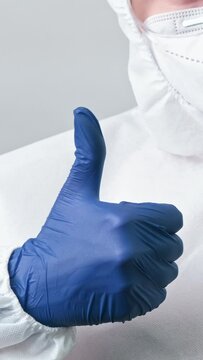 Vertical video. Successful treatment. Like gesture. Healthcare doctor specialist in white medical suit mask with blue glove hand thumb up sign.