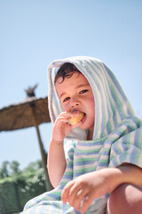 Summer fun: little child in the pool, covered in a towel and enjoying a corn snack