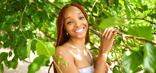 Close up portrait Beautiful young African American woman with red braids hair, perfect white teeth smiling outside, sunny summer day green foliage. Facial treatment. Cosmetology, skin care and spa - obrazy, fototapety, plakaty