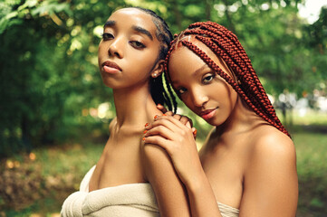 Fashion Close up outdoor portrait Beautiful young African American female couple with braids hair posing at sunny summer day green foliage. Cosmetology, perfect skin care, spa. Natural face treatment - obrazy, fototapety, plakaty