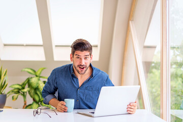 Happy businessman using laptop and shought with joy at office desk