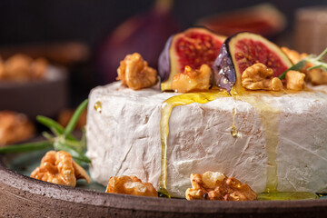 Camembert cheese with fig fruits, honey, walnuts and rosemary on dark background. French appetizer. Close up