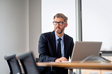 Mid aged man with laptop sitting in the office and looking thoughtfully