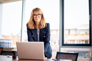 Mid aged woman standing at the office and using laptop for work