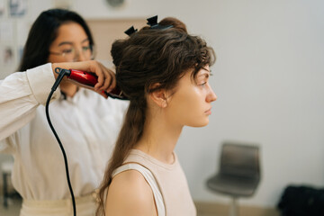 Closeup side view of professional female hairstylist using hair iron and comb for woman hairstyling...