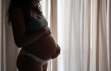 Backlight of pregnant woman in front of curtains