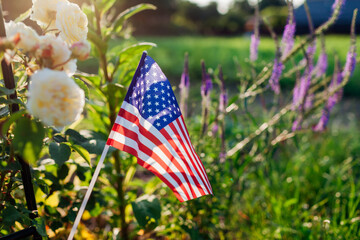 Independence day of USA. American flag put in summer garden by flowers at sunset. July 4th. Memorial day