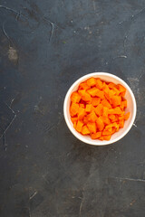 Above view of chopped fresh carrots in a white bowl on the left side on dark color table with free space