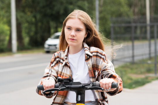 young woman on an electric scooter rides down the street - Powered by Adobe