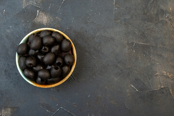 Above view of fresh black olives in a white bowl onthe right side on dark color table with free space