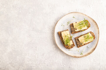 Grain bread sandwiches with cheese and watercress microgreen on gray concrete, top view, copy space.