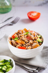 Hearty salad of pasta, cherry tomatoes, cucumbers and fried bacon in a bowl vertical view