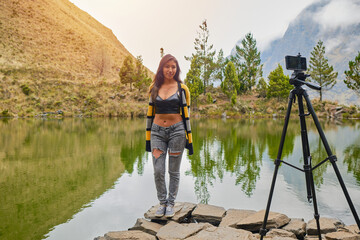 young latina woman recording a video for her social networks in a lake surrounded by mountains in la paz bolivia - obrazy, fototapety, plakaty