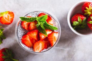 Close up of chia seeds pudding with fresh strawberry pieces and mint in a glass top view