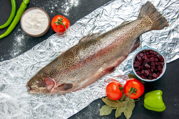 Above view of scales removed fresh fish vegetables flour in a bowl on dark color background