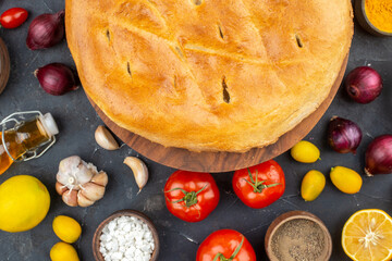 Above view of freshly-baked bread among fresh vegetables fallen oil bottle spices eggs on dark color background