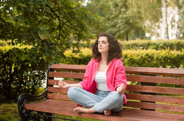 Girl does yoga in an outdoor summer park. Performs exercises to restore strength and spirit meditates, feeling Zen-style in a public park