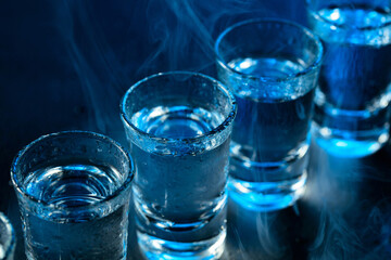 Wet glasses of vodka in smoke on dark blue background.