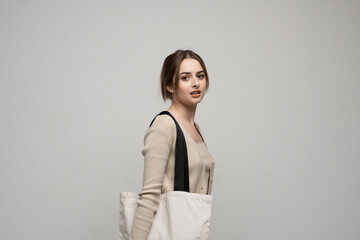 Cheerful millennial woman with a white eco bag standing over white studio background. Lady holding shopper handbag. Fashion and ecology concept, Selective Focus. No more plastic.