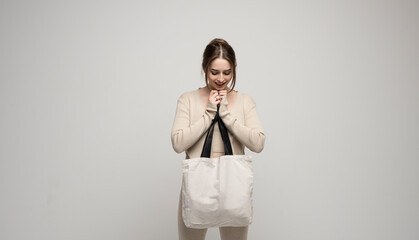 Young happy and excited woman in beige costume with white cotton bag in a hand. Mockup and zero waste concept.