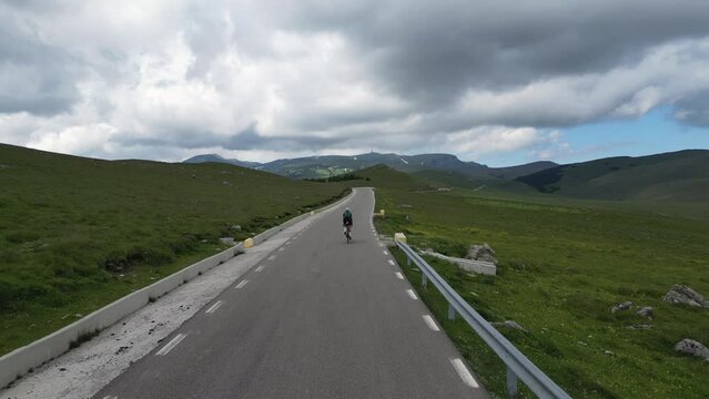 Aerial view video of a female cyclist riding on a road bicycle. The cyclist is pictured on an empty road that passes through mountains in the Bucegi National Park.Cycling adventure in Romania 