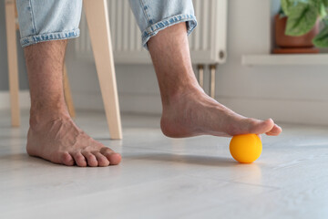 Man using silicone ball for foot massage during long sedentary work, legs close-up. Physical...