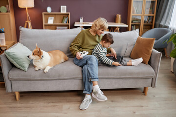 Full length portrait of mother and son with down syndrome watching videos via laptop together while sitting on sofa in cozy home