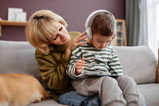 Loving mother putting headphones on little boy with down syndrome using laptop at home
