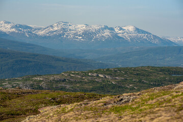 View over nordic mountain peaks in Norway from a hike up Hauknestinden, Hauknes, Mo i Rana, Helgeland, Norway. High peaks in a fjord landscape, snow covered. Clear Norwegian summer skies. Wild Norway
