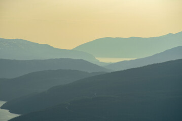 View over nordic mountain peaks in Norway from a hike up Hauknestinden, Hauknes, Mo i Rana, Helgeland, Norway. High peaks in a fjord landscape, snow covered. Clear Norwegian summer skies. Wild Norway