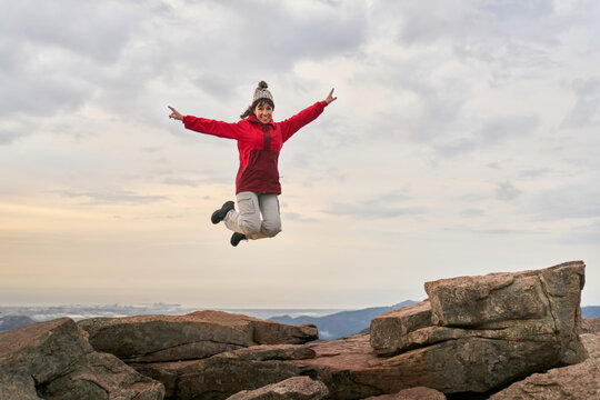 Carefree woman jumping on mountain cliff during sundown - Powered by Adobe