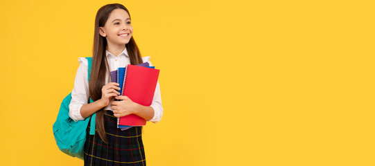happy child with backpack and workbook in school uniform full length on yellow background, education. Portrait of schoolgirl student, studio banner header. School child face, copyspace. - obrazy, fototapety, plakaty