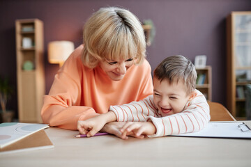 Front view portrait of happy little boy with down syndrome studying and having fun with mother or...