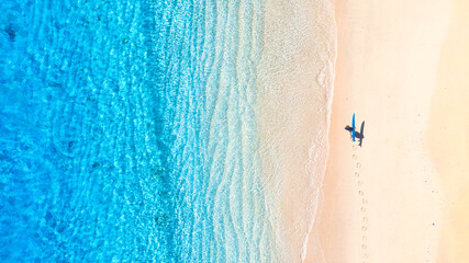 Surfer with a board on the beach. Blue water and clean beach in the summer. View from a drone. An aerial view of the seascape. Recreation and active sports. - 619231699