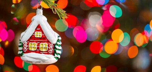 Christmas tree decorated red toy house, Fir branch with red toy house and festive lights on the Christmas background with sparkles and bokeh
