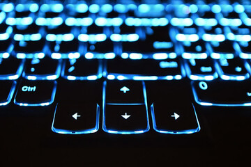 Notebook keyboard with backlight turned on at night. Blue laptop backlit keyboard. Cursor keys in the foreground
