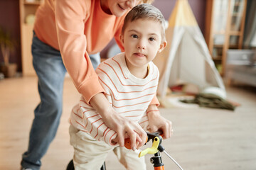 Portrait of little boy with down syndrome playing with runbike and looking at camera