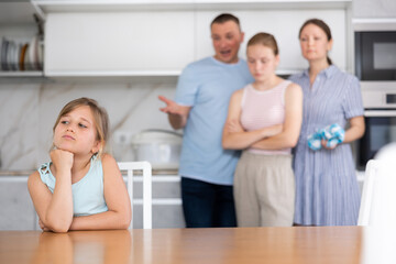 Parents scold child for bad behavior at school. Eldest daughter sits sullenly at table and listens to complaints from parents, edifying advice.