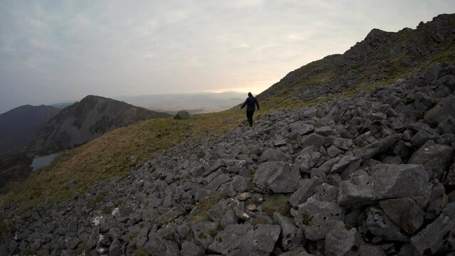 A figure walking over rocks towards a wild camping tent in the mountains of Wales